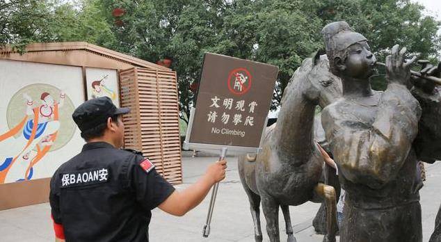 游客攀爬景区的雕塑拍照，保安喊话劝告无效，沉默地递上一牌子