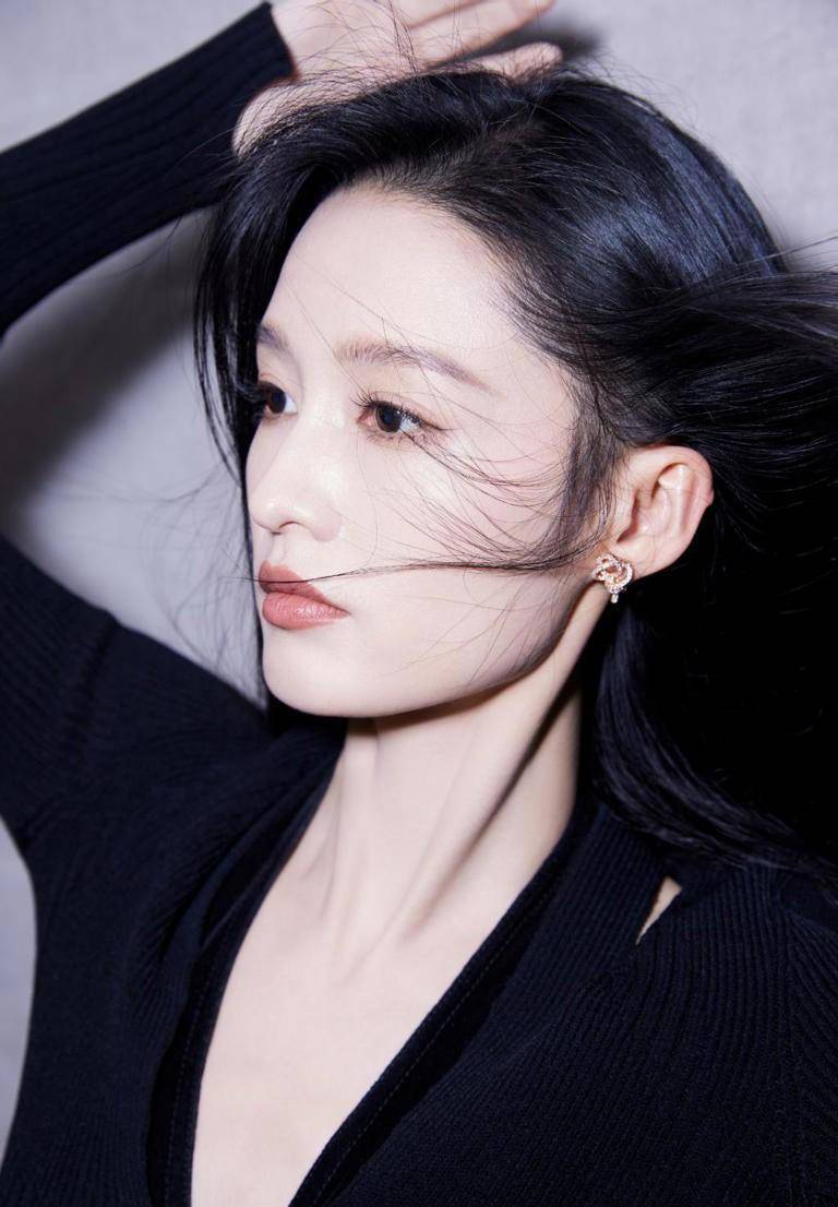 李沁的长发飘扬,他身穿深v黑色上衣,手捧鲜花看着镜头,他大胆又美丽