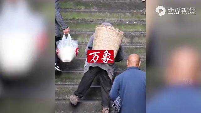 老人拄著柺杖艱難爬樓梯揹著籮筐且停且走雨中前行令人心酸