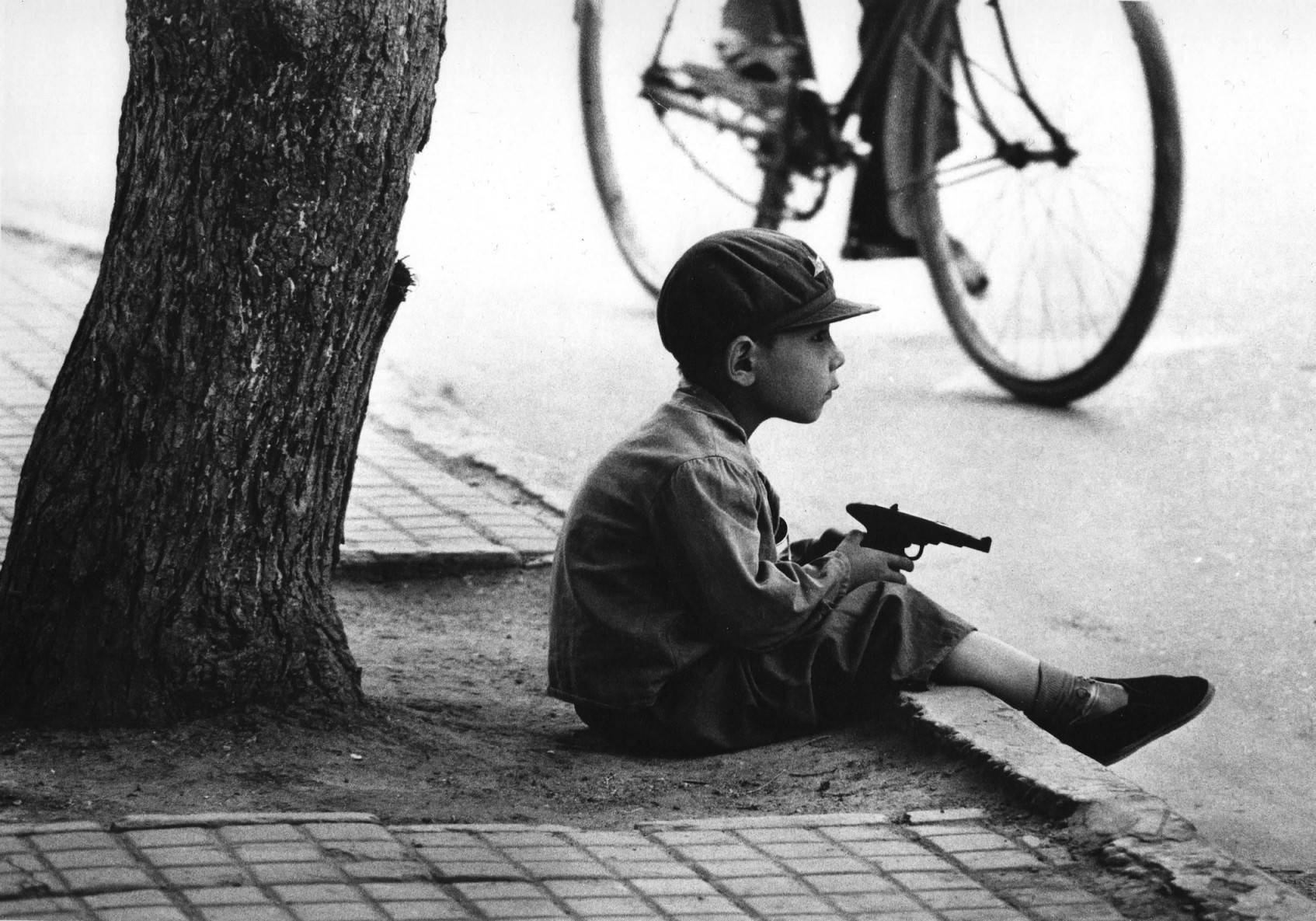 由外国摄影家volker hinz拍摄,在街头,戴着军帽的小男孩坐在路牙上