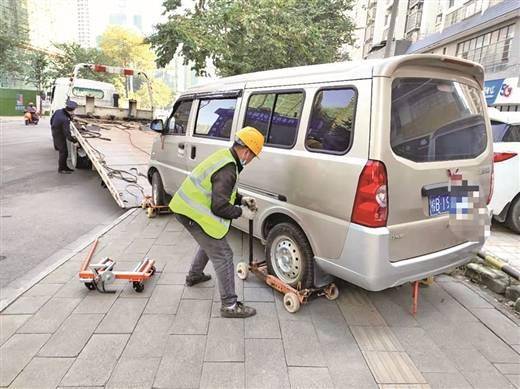 城管队员用万向轮成功拖移一辆紧挨路肩违停的面包车.