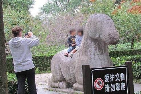 妈妈抱小孩坐在石雕上拍照，对旁边指示牌“请勿攀爬”视而不见